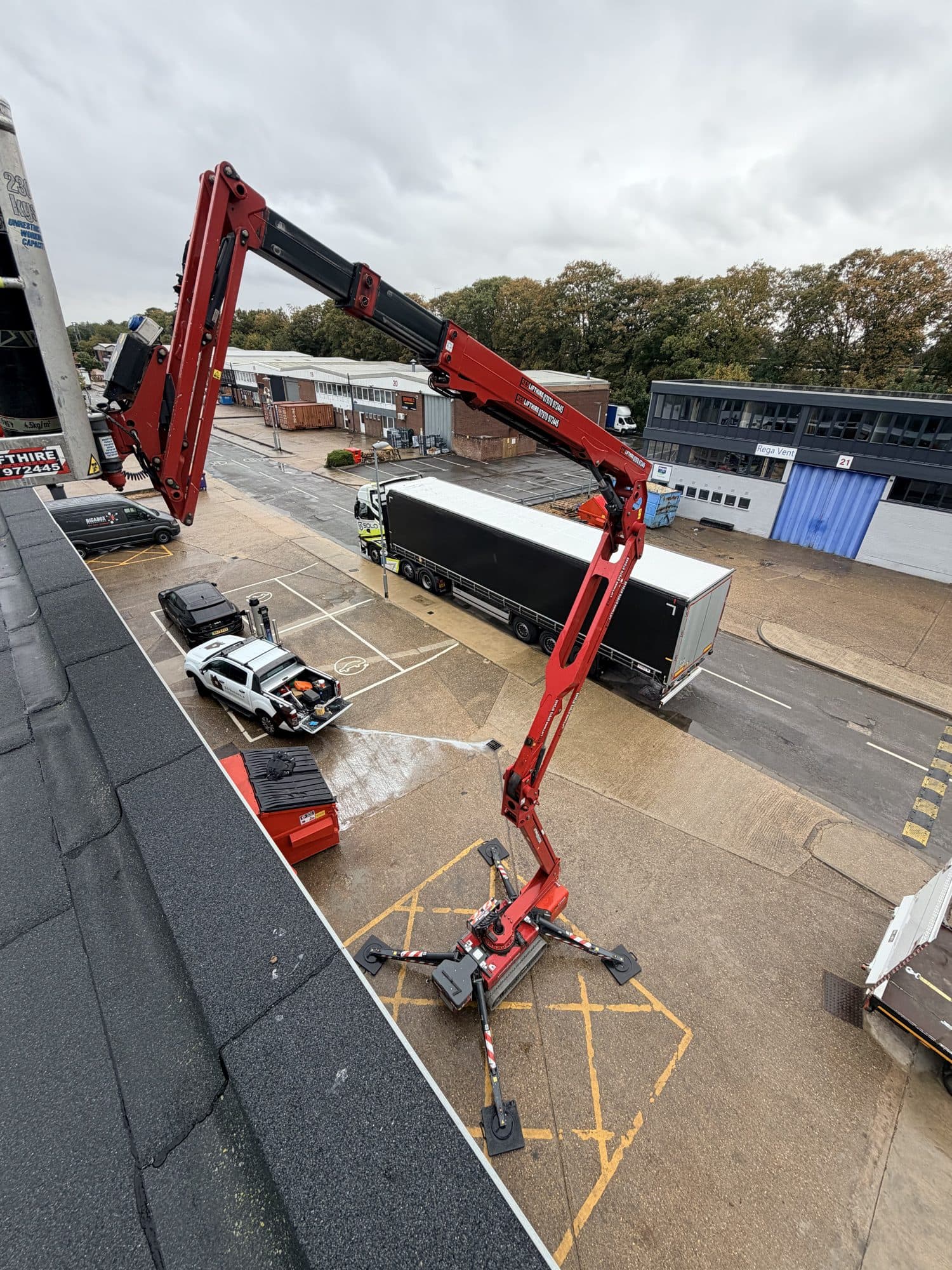 Cherry picker access platform raised to roof level at a commercial unit, with lorries and vans parked in the yard below, Eldon Way, Biggleswade