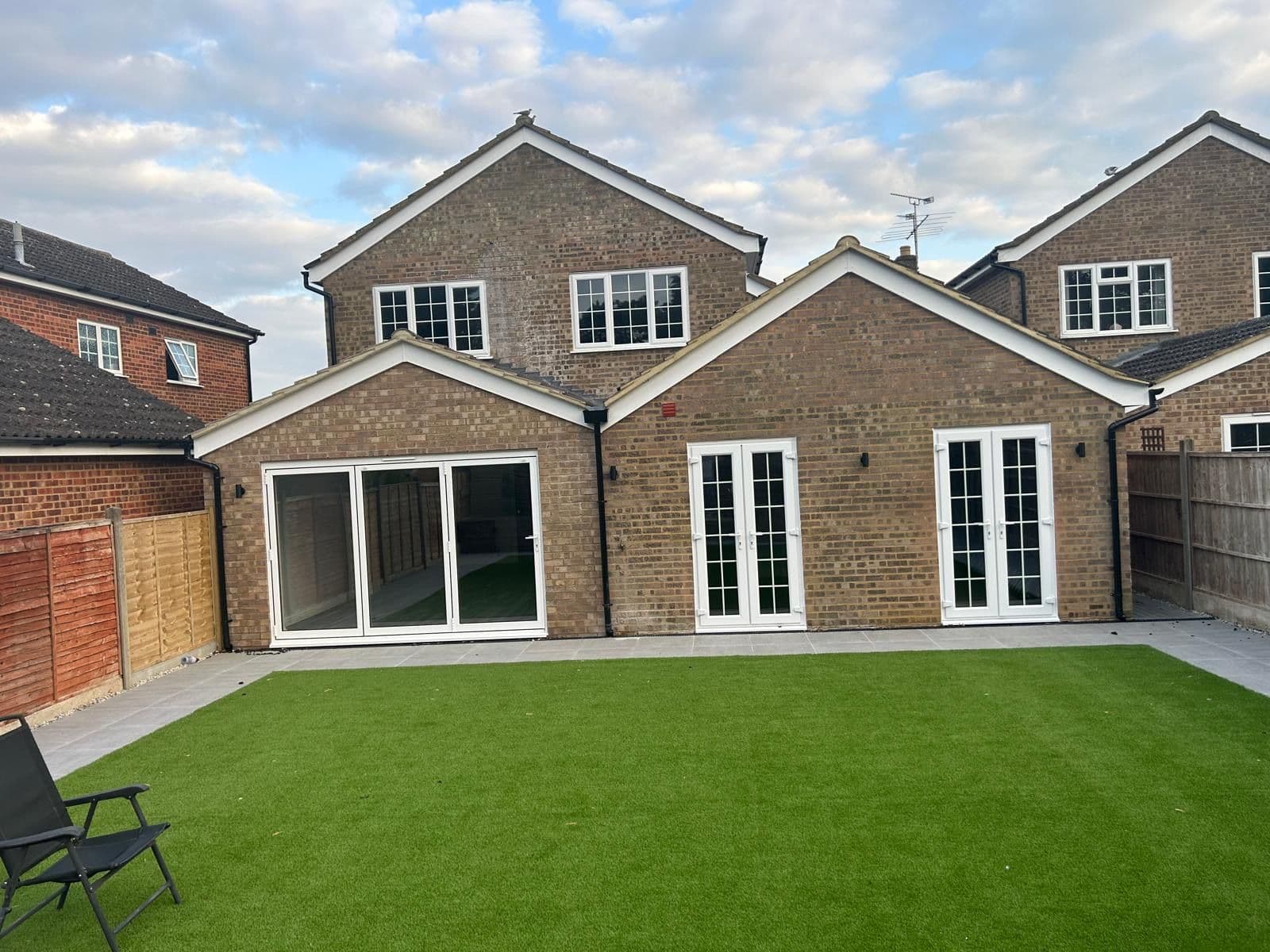 Rear of extended house with brown brickwork, bifold and French doors onto a garden with artificial lawn, Taddy Close, Upper Caldecote